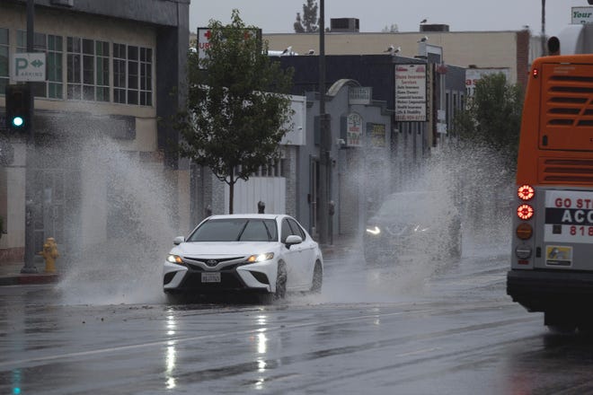 A vehicle splashes through puddles along a street starting to flood in the Van Nuys section of Los Angeles as a tropical storm moves into the area on Sunday, Aug. 20, 2023.