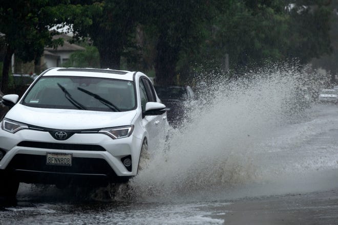 A vehicle makes its way through a flooded street in a suburban area of the San Fernando Valley in Los Angeles as a tropical storm moves into the area on Sunday, Aug. 20, 2023.
