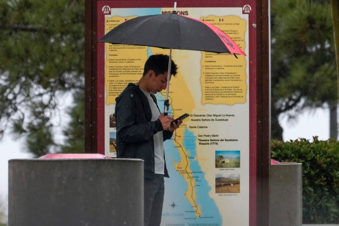 A motorist checks his phone in the rain at a rest stop in Oceanside, Calif., Sunday, Aug. 20, 2023.