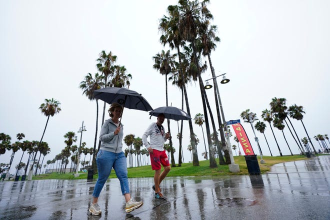 People walk along Venice Beach in the rain, Sunday, Aug. 20, 2023, in Los Angeles.