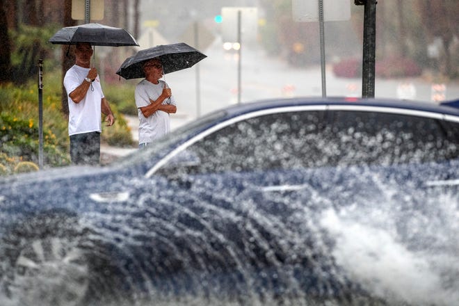 Jeff Larsen, left, and Robbie Jones watch cars drive on flooded streets during Tropical Storm Hilary in Palm Springs, Calif., on Sunday, August 20, 2023.